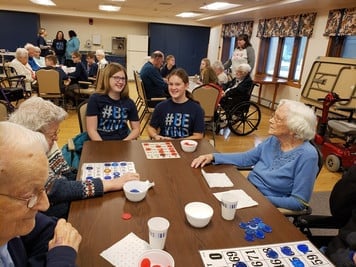 Senior citizens and students play bingo at table