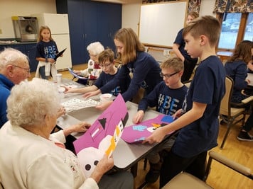 Elderly woman cutting out an art project of a snowman with students