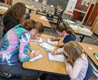 Table of four girls leaning over writing letters