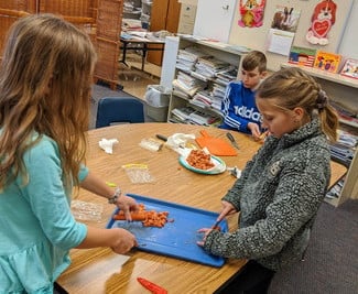 Two girls cutting food items on a table